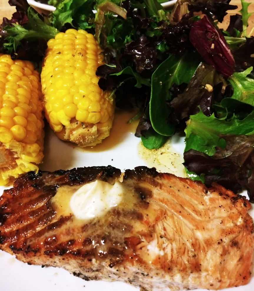 Grilled salmon dinner with corn cobbettes and mixed green salad.